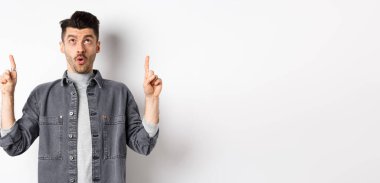 Heyecanlı, kot ceketli, yukarı bakan, nefes nefese kalmış, havalı teklifleri kontrol eden, beyaz arka planda duran modern adam..