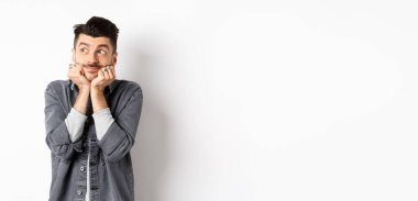 Heyecanlı genç adam sol üst köşede rüya gibi görünüyor, paketi bekliyor, hayal görüyor ya da hayal kuruyor, beyaz arka planda duruyor..