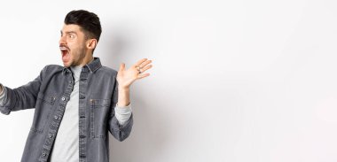 Şaşırmış ve kafası karışmış bir adam akıllı telefon ekranına bakıyor, hayal kırıklığından bağırıyor, beyaz arka planda duruyor..