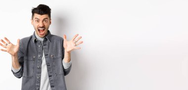 Kızgın adam çığlık atıyor ve kameraya bakıyor, öfkeli ve nefret dolu bir ifadeyle bağırıyor, beyaz arka planda duruyor..