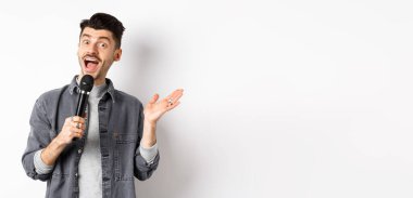 Heyecanlı stil sahibi adam konuşma yapıyor, mikrofonla konuşuyor, karaoke yapıyor ya da şarkı söylüyor, beyaz arka planda duruyor..