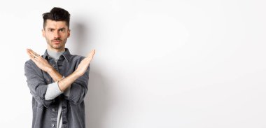 Kızgın adam durmak ya da hayır demek için çapraz hareket gösterir, kaşlarını çatar ve ciddidir, aynı fikirde değildir ve kötü durumu engeller, beyaz arka planda durur..