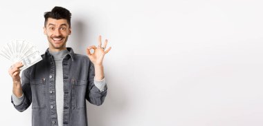 Dolarları tutan heyecanlı bir adam resmi ve mutlu yüzle işaret göster, para kazan, beyaz arka planda dur..