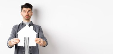 Gayrimenkul ve sigorta konsepti. Kararsız adam düşüncelere dalıp gazete kupürlerini gösteriyor. Mülk almayı düşünüyor, beyaz arka plana karşı duruyor..