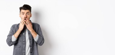 Şok olmuş, beyaz adam soluk soluğa kalmış, ağızını ellerle kapatmış ve korkunç bir şeye bakıyor, kötü bir kazaya tanık oluyor, aman Tanrım, beyaz arka planda duruyor..