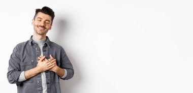 Romantik, mutlu bir adam kalbi kucaklıyor ve kapalı gözlerle gülümsüyor, bir şeyin hayalini kuruyor, tatlı anılardan nostalji hissediyor, beyaz arka planda duruyor..