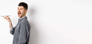 Mutlu adam kameraya bakarken ses çevirici uygulamasını kullanıyor ya da hoparlörden konuşuyor, telefonu ağıza yakın tutuyor, beyaz arka planda duruyor..