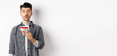 Yakışıklı doğum günü çocuğu pastaya mum üflüyor ve dilek tutuyor, kameraya bakıp, beyaz arka planda duruyor..