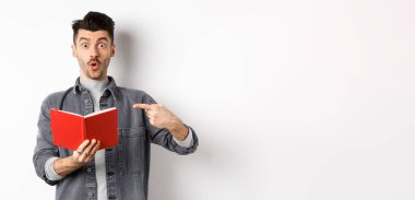 Heyecanlı adam günlükte ilginç bir şey okudu, planlayıcıyı işaret etti ve etkilenmiş görünüyordu, beyaz arka planda duruyordu..