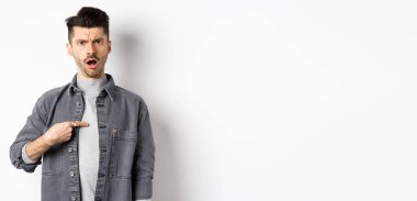 Genç bir adamın suçlanması, kaşlarını çatması ve kendini göstermesi, şok olması, beyaz arka planda durması rahatsız edici..