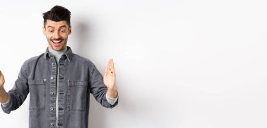 Heyecanlı beyaz adam büyük bir nesne gösteriyor, büyük bir şey şekillendiriyor ve şaşırmış bir şekilde gülümsüyor, beyaz arka planda duruyor..