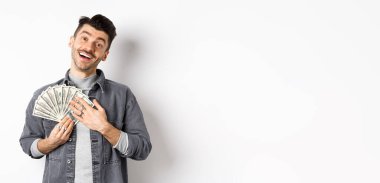 Mutlu gülümseyen adam para kazanıyor, mutlu yüzle dolarları kucaklıyor, beyaz arka planda duruyor..