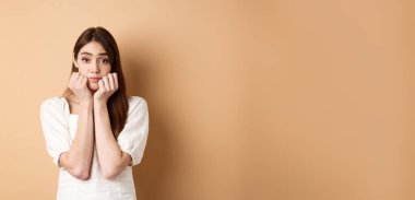 Sevimli ve aptal bir kız ellerinde sıska bir yüz ve kameraya hayalperest bakıyor, bej arka planda romantik duruyor..