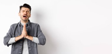 Sefil bir adam yardım için yalvarıyor, bir şeye ihtiyacı var ve ağlıyor, üzgün bir yüzle yalvarıyor, beyaz arka planda çaresizce duruyor..