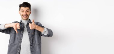 Mutlu gülümseyen adam ortalama bir hareket gösteriyor, baş parmağını kaldırıyor, karar veremiyor, bir şeyi orta derecede yargılıyor, beyaz arka planda duruyor..