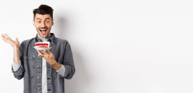 Doğum gününü kutlayan heyecanlı adam, mumla doğum günü pastasına mutlu bakıyor, dilek diliyor, beyaz arka planda mutlu duruyor..