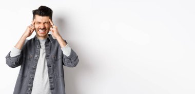 Baş ağrısı çeken, baş ağrısından dişlerini sıkan, baş şakaklarına dokunan, migren ağrısı çeken, beyaz arka planda duran, ağrı kesicilere ihtiyacı olan bir adam..