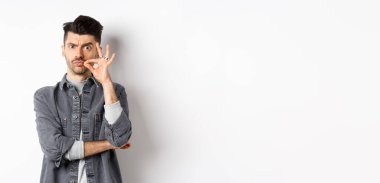 Ciddi adam fermuar hareketi yapıyor, çenesini kapalı tutmasını söyle, kaşlarını çatsın ve dudaklarını mühürlesin, beyaz arka planda dursun..