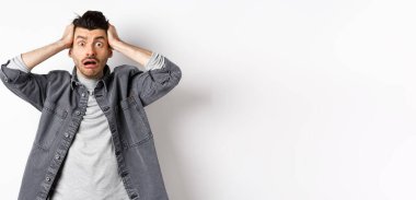 Telaşlı genç adam kameraya bakıyor, endişeli ve sıkıntılı görünüyor, büyük bir problemi var, beyaz arka planda panikliyor..