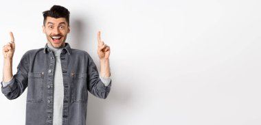 Heyecanlı yakışıklı adam parmak kaldırıyor, gülümsüyor, mutlu ve özel bir anlaşma yapıyor, beyaz arka planda duruyor..