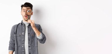 Heyecanlı adamın görüntüsü büyüteçten bakıyor, hayret içinde, büyük göz ilginç bir şeye bakıyor, havalı bir reklam buluyor, beyaz arka planda duruyor..