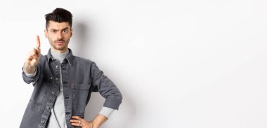 Burada dur. Ciddi bir adam azarlıyor, parmağını sallıyor, kaşlarını çatıyor, kötü bir şeyi onaylamıyor, beyaz arka planda duruyor..