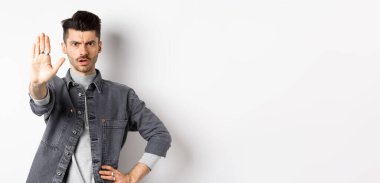 Ciddi bir adam durmasını, bir şeyi yasaklamasını ve kaşlarını çatmasını söyler, hayır der, elini beyaz arka plana uzatmaktan rahatsız olur..