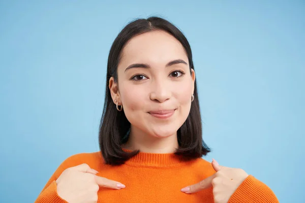 stock image Close up of confident smiling korean girl, points at herself with pleased, satisfied face, stands over blue background. Copy space