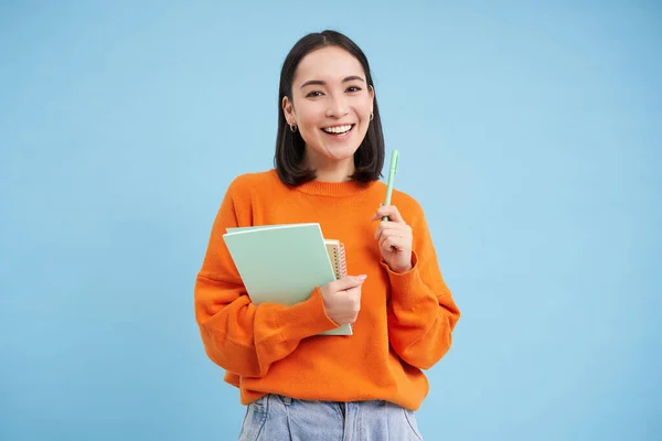 Smiling asian woman with notebooks, student with happy face, promo of college education, blue background.