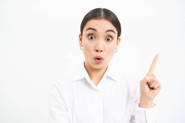 Başarılı Koreli iş kadını, sağı işaret ediyor, afişte reklamını gösteriyor, beyaz arka planda duruyor..