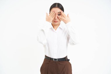 Genç Asyalı kadının portresi elleriyle gözlerini kapatıyor, bir şeyden saklanıyor, beyaz arka plan..