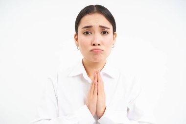 Üzgün genç satıcı, Asyalı kadın dua etmek için el ele tutuşuyor, sana yalvarıyor, üzgün bir yüzle yardım istiyor, yalvarıyor, beyaz arka planda duruyor..