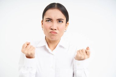Portrait of angry, pissed-off businesswoman, japanese lady clenches fists and looks up with bothered, frustrated face expression, standing over white background.