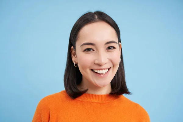 Close up portrait of beautiful korean woman with healthy smile, natural clear facial skin, stands over blue background.