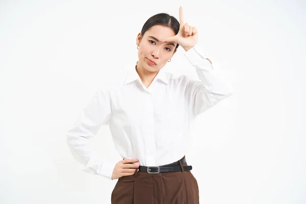 stock image Successful businesswoman looks confident, shows L letter, loser sign on forehaed, feels proud of herself, smiles pleased over white background.