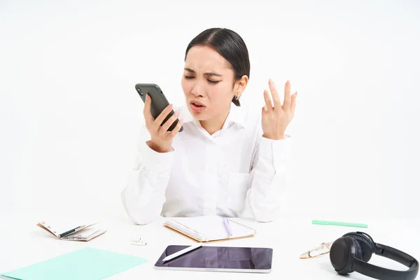 Angry lady boss, businesswoman looks frustrated, talks on mobile phone, has an argument during conversation on cellphone, sits in her office, white background.