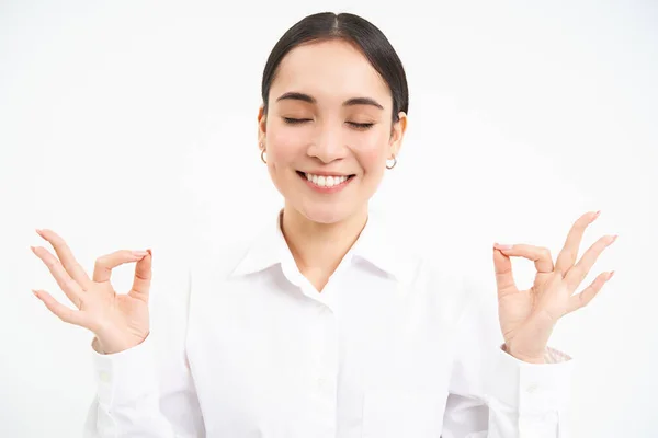 stock image Asian business woman meditates, keeps patience, calms down, breathes in and out, relaxes after stressful day at work, stands over white background.