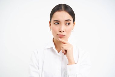 Asyalı bayan patronun düşüncesine göre, iş kadını portresi, düşünceli görünüyor, ciddi yüzlü bir şey düşünüyor, beyaz arka planda duruyor..