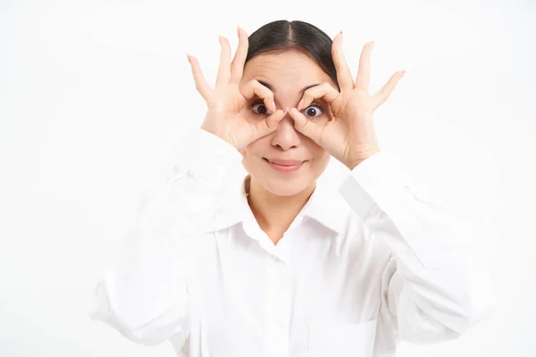 stock image Business people. Happy asian girl looks through finger glasses, stares with surprised face, stands isolated on white background.