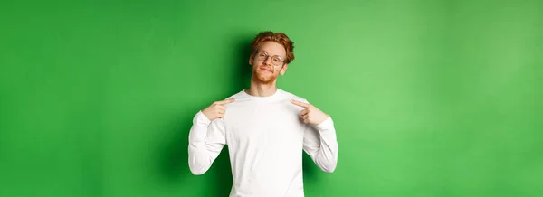 自信而沾沾自喜的红头发男人 戴着眼镜笑着 指着自己自信 站在绿色的背景之上 复制空间 — 图库照片