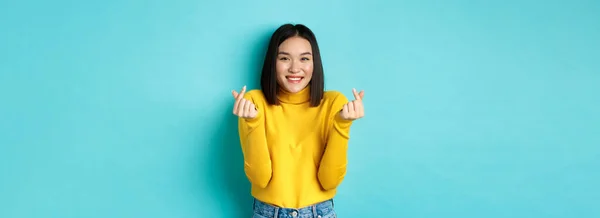 Piękna Azjatycka Dziewczyna Żółtym Swetrze Uśmiechnięta Pokazująca Palcem Serca Stojąca — Zdjęcie stockowe