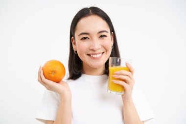 Gülümseyen Asyalı kadın taze portakal suyu içiyor ve elinde meyve tutuyor, aktif ve sağlıklı bir hayat sürüyor, beyaz bir geçmişi var..