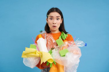 Farklı tipte plastikleri olan kafası karışmış genç Asyalı kız, geri dönüşüm yapmayı, çevreyi korumayı, çöpleri ayırmayı, mavi arka planı öğreniyor..