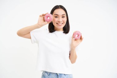 Komik gülümseyen Koreli kadın, elinde iki tane jöleli pembe çörek, gülen yüzlü tatlı yiyor, beyaz bir geçmişi var..