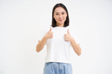 Hevesli Asyalı kız başparmağını kaldırır, beğenir ve onaylar. Yumuşak, olumlu geri bildirim, onay, kafa sallama ve gülümseme, beyaz arka plan..