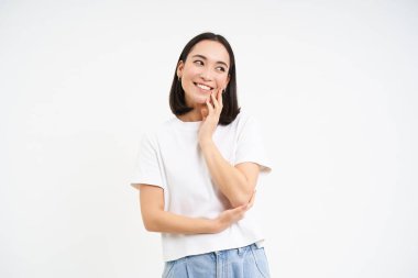 Şefkatli, sevimli Asyalı bir kadının portresi, flört eden, aptal bir yüz ifadesiyle beyaz arka planda duran.