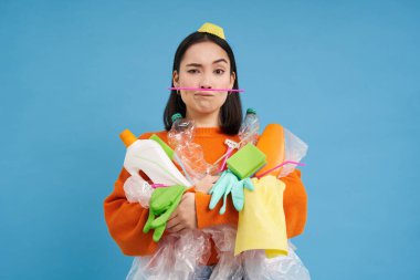 Çevre ve ekoloji. Plastik atık taşıyan Asyalı kadın portresi, çöp yığını, mavi arka plan.