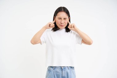 Sinirli Asyalı kadın, yüksek sesten parmaklarıyla kulaklarını kapatır, sese dayanamaz, beyaz arka planda durur..