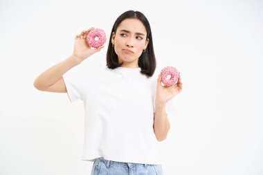 Düşünceli Koreli kadın, elinde iki tane jöleli çörek tutuyor, düşünüyor, diyette, beyaz stüdyo geçmişi var..