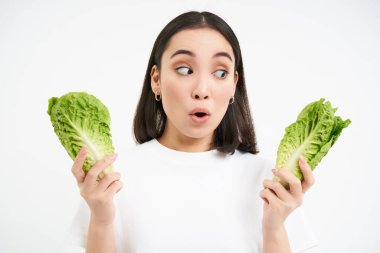 Şaşırmış yüzlü bir kadın portresi, elinde lahana, marul yaprakları, ve şaşkın görünüyor, kendi bahçesinde sebze yetiştiriyor, beyaz arka plan.